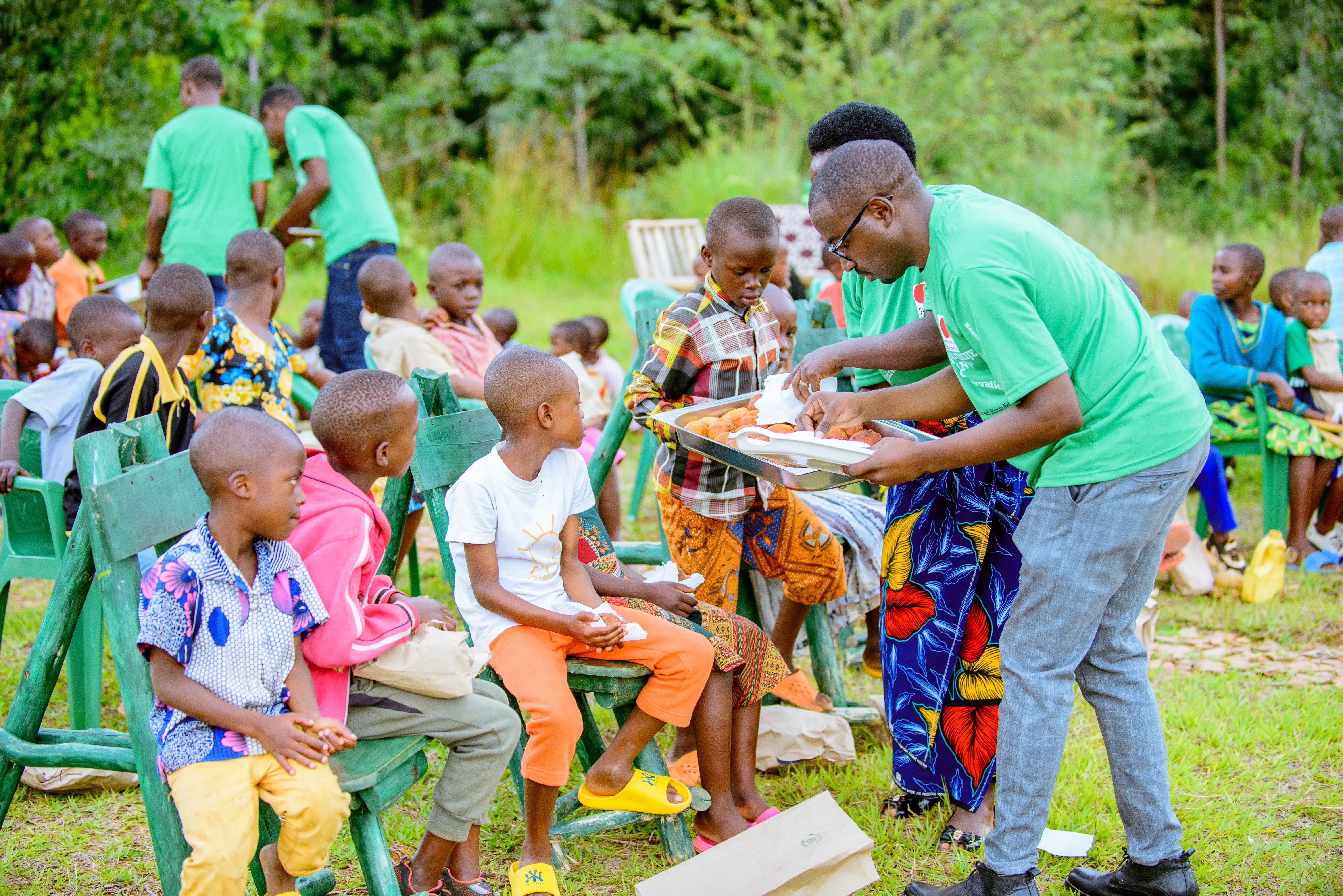 A rwandan men serving food to rwandan children outdoors